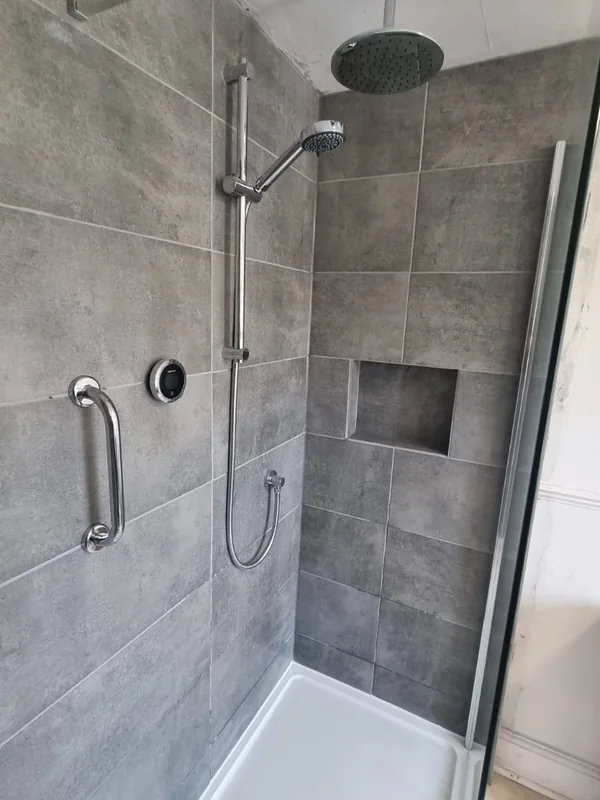 Grey tiled shower enclosure with a chrome rainfall head, riser rail, grab rail and a recessed tiled shelf